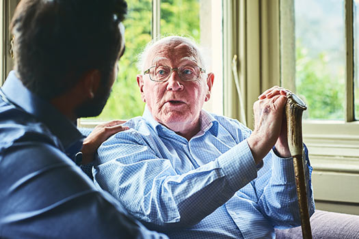 Senior man leaning on his cane speaking with young man in his assisted living home. 