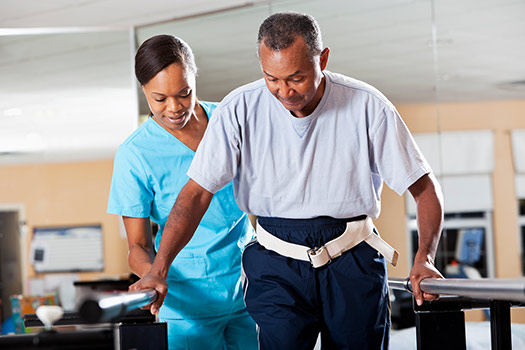 Senior man walking during physical therapy using a gait belt with therapist behind him, offered through skilled nursing at Fellowship Square.