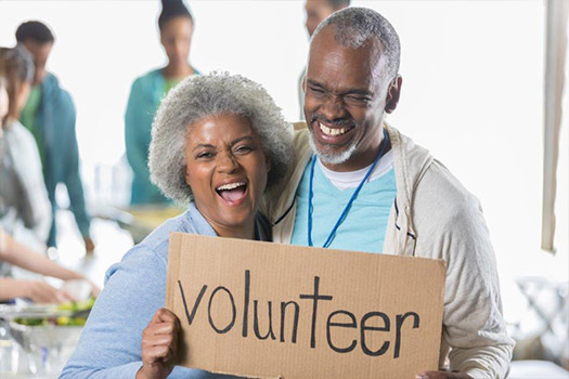Black senior couple holding volunteer sign - many residents at Fellowship Square give back by volunteering